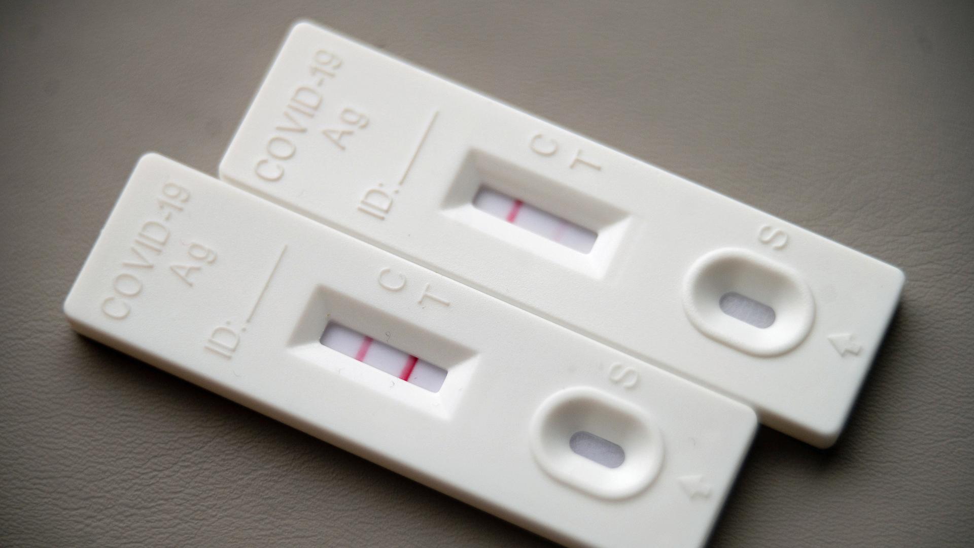 Ein positiver Corona-Schnelltest (l.) liegt auf einem Tisch neben einem Corona-Schnelltest, der schwach eine positive Linie hat. | Sebastian Gollnow/dpa 