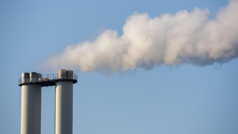 Industrieschornsteine mit ausstoßendem Rauch gegen blauen Himmel.