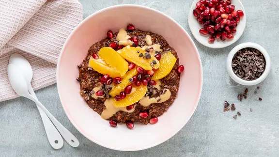 Eine Schale mit einem dunklen Porridge, darauf Orangenscheiben und Granatapfelkerne. | ZS-Verlag, Claudia Timmann Eine Schale mit einem dunklen Porridge, darauf Orangenscheiben und Granatapfelkerne.