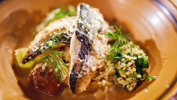 Gebratene Makrelenfilets mit Sauerkraut-Bouillon und Graupen auf einem Teller serviert.