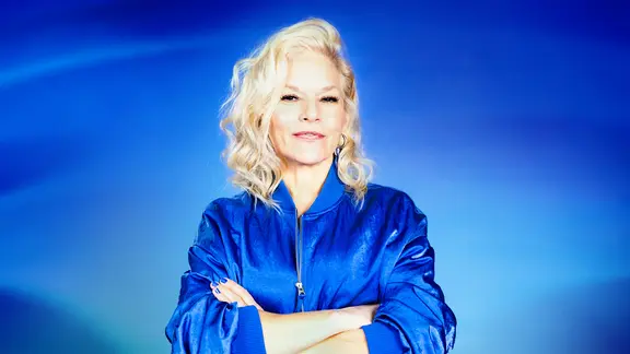 Ina Müller lächelt mit verschränkten Armen in die Kamera.