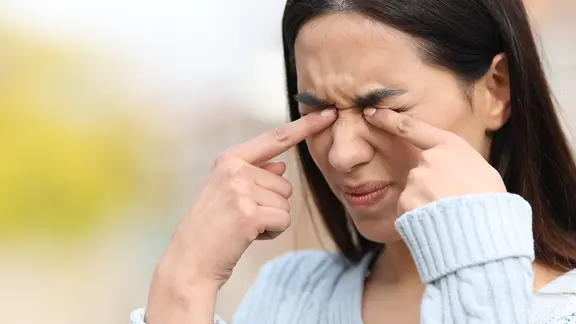 Junge Frau reibt sich mit beiden Zeigefingern zugleich die zusammengekniffenen Augen.