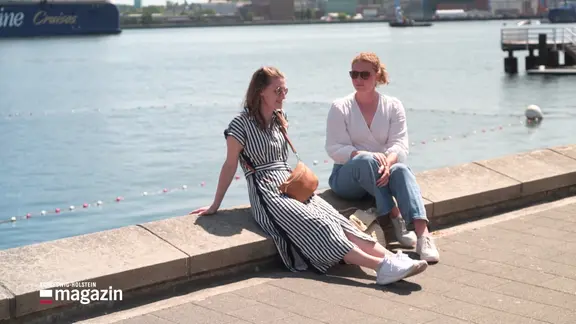 Zwei Personen sitzen an der Hafenpromenade in Kiel.