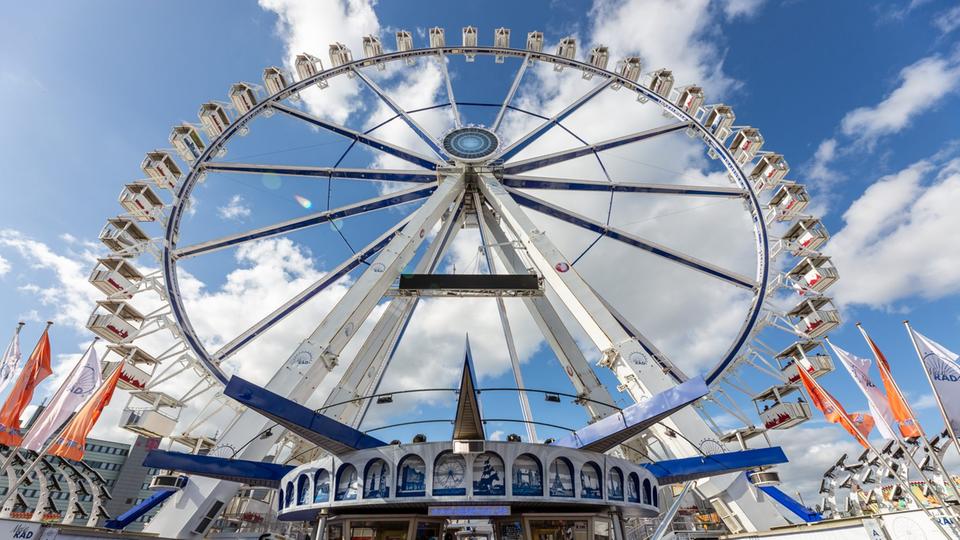 Großes Riesenrad mit Rollstuhl-Gondel auf der Kieler Woche. | MeinRad Man sieht ein großes Riesenrad. Davor stehen einige Menschen.