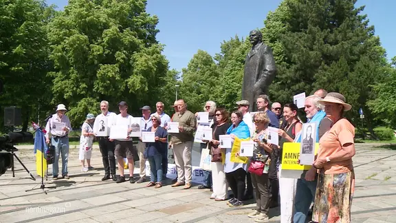 Mehrere Demonstrierende posieren für ein Gruppenfoto vor einem Denkmal Lenins.
