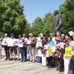 Mehrere Demonstrierende posieren für ein Gruppenfoto vor einem Denkmal Lenins.