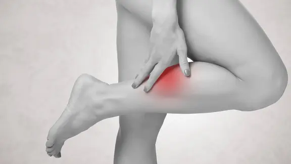 Eine Frau hält sich den Unterschenkel. Eine stelle der Wade ist rot markiert.