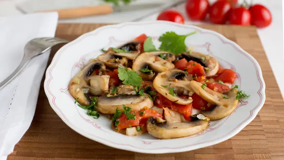 Gebratene Tomaten und Champignons auf einem Teller auf einem Holzbrett