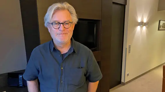 Bent Hamer steht in einem Flur und lächelt in die Kamera. 