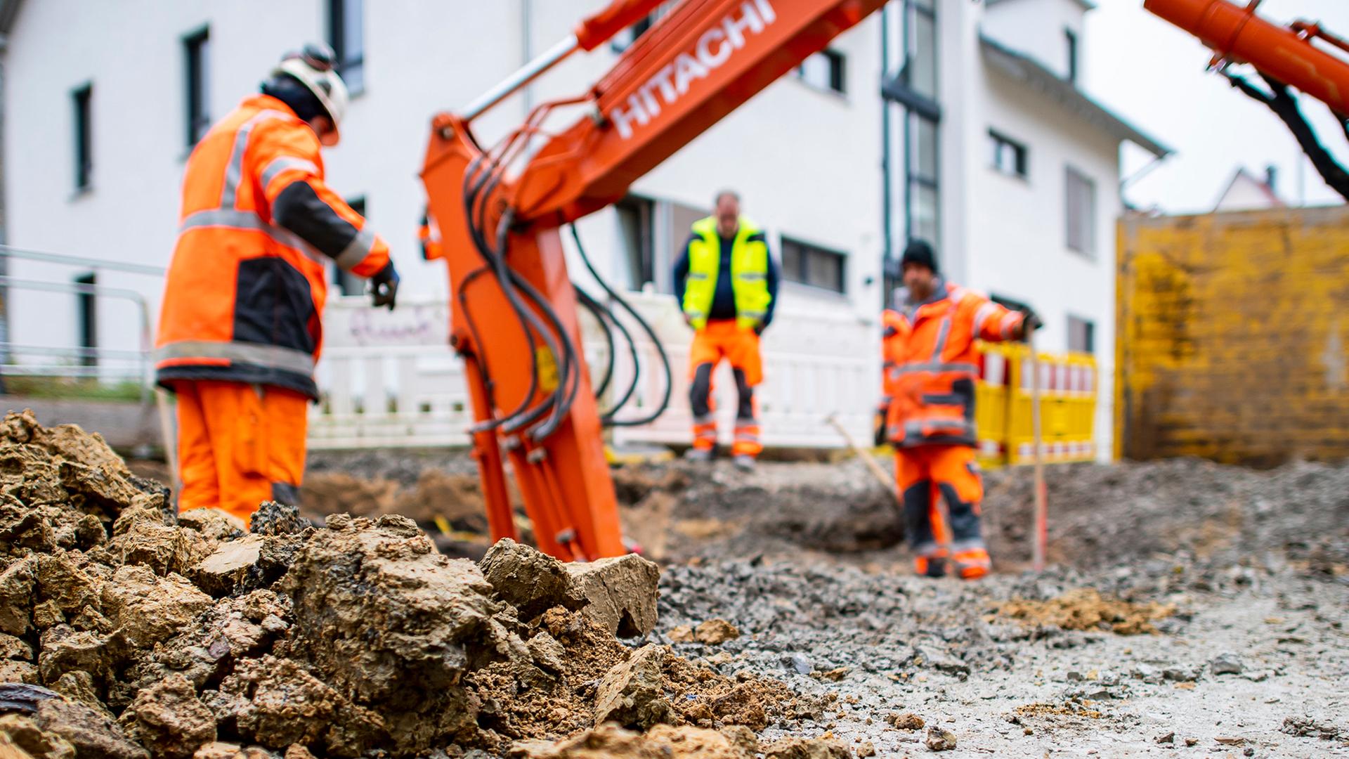 Drei Bauarbeiter auf einer Baustelle mit einem Schaufelbagger. | dpa-Bildfunk, David Inderlied