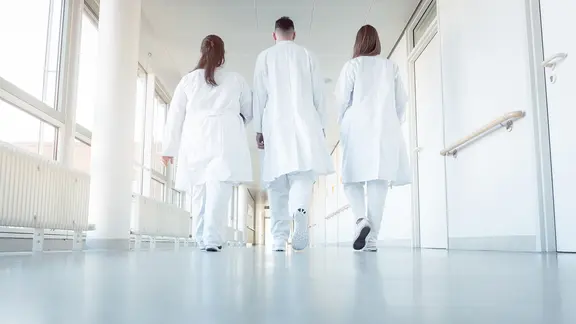 Zwei Ärztinnen und ein Arzt gehen auf einem Krankenhausflur entlang