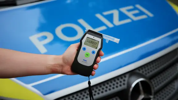 Ein Polizist hält ein einsatzbereites Atemtestgerät vor der Motorhaube eines Streifenwagens.