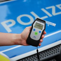 Ein Polizist hält ein einsatzbereites Atemtestgerät vor der Motorhaube eines Streifenwagens.