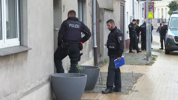 Polizisten stehen vor einer Haustür in einer Straße in Güstrow. | Stefan Tretrop Polizisten stehen vor einer Haustür in einer Straße in Güstrow.