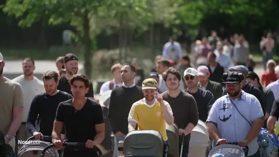 Ein Männergruppe schiebt Kinderwägen an der Alster entlang.