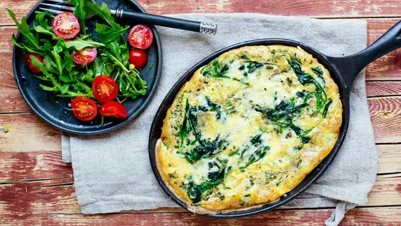 Ein Teller mit Rukolasalat und eine Pfanne mit Spinatomelett stehen auf dem Tisch.
