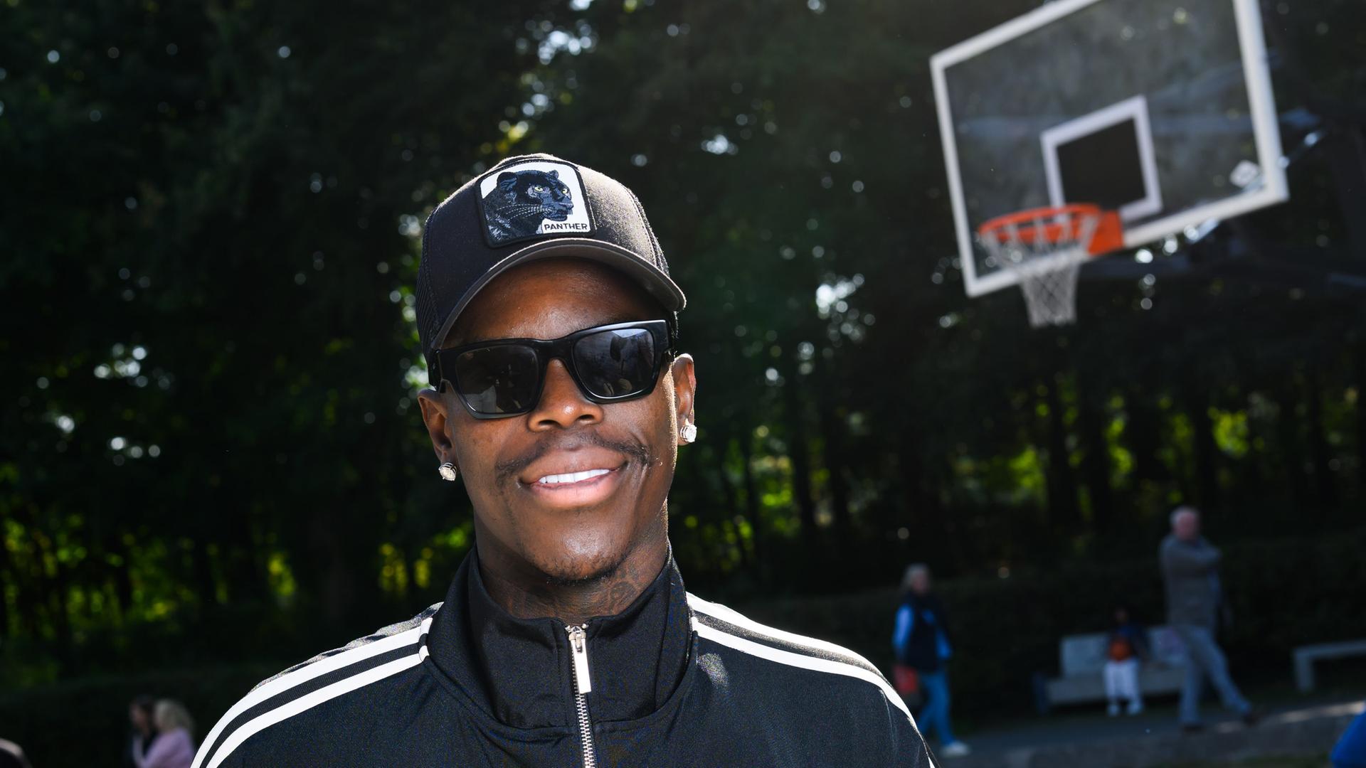 Dennis Schröder steht im Prinzenpark vor einem Basketballkorb. Er trägt Cap und Sonnenbrille. | picture alliance/dpa