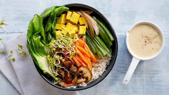 Eine Schale mit Reis und viel Gemüse, daneben ein weiteres kleines Schälchen.  