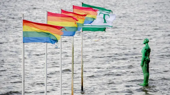 Fahnen wehen bei stürmischem Wetter am Strand vor dem Jadebusen und der Figur "Die grüne Nackte".