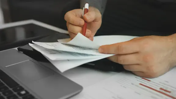 Ein Mann sitzt am Schreibtisch und sieht sich Unterlagen mit einem Stift an. | Colourbox, M-production Ein Mann sitzt am Schreibtisch und sieht sich Unterlagen mit einem Stift an.