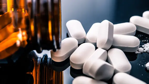 Tabletten aus einem Glasfläschchen ergießen sich auf schwarzen Tisch (Bild: colourbox.de)
