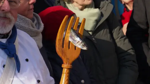 Ein Hering, aufgespießt auf einer überdimensional großen Holzgabel.