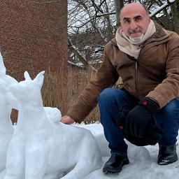 Ein Mann kniet neben einer Skulptur aus Schnee von einer Frau und einem Hund