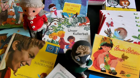 Οι φιγούρες του Sandman και του Pittiplatsch στέκονται σε μια στοίβα παιδικών βιβλίων