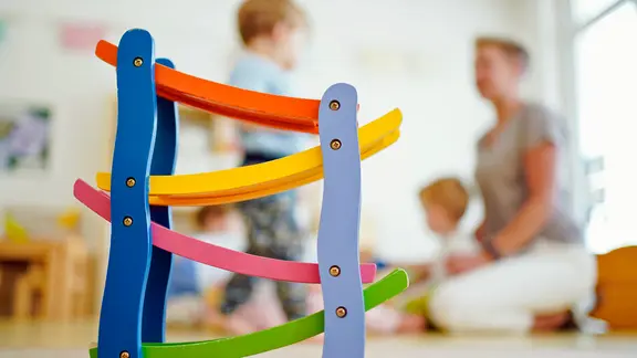 Eine Erzieherin spielt in einer Kindertagesstätte hinter einer Rollbahn mit Kindern. 