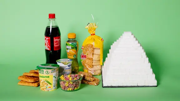 Eine Pyramide aus Zuckerwürfeln steht neben Cola, Toasties, Waffeln und anderen Fertigprodukten.