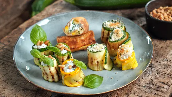 Zucchini-Röllchen mit Ricotta-Füllung auf einem blauen Teller