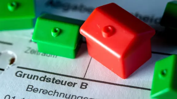 Kleine Spielzeughäuser aus Kunststoff stehen auf einem Abgabenbescheid für die Entrichtung der Grundsteuer. In die zähen Verhandlungen von Bund und Ländern über eine Reform der Grundsteuer hat Schleswig-Holstein einen neuen Kompromissvorschlag eingebracht.