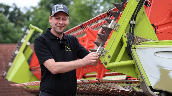 Ein Landwirt steht an einem Mähdrescher und schaut in die Kamera.