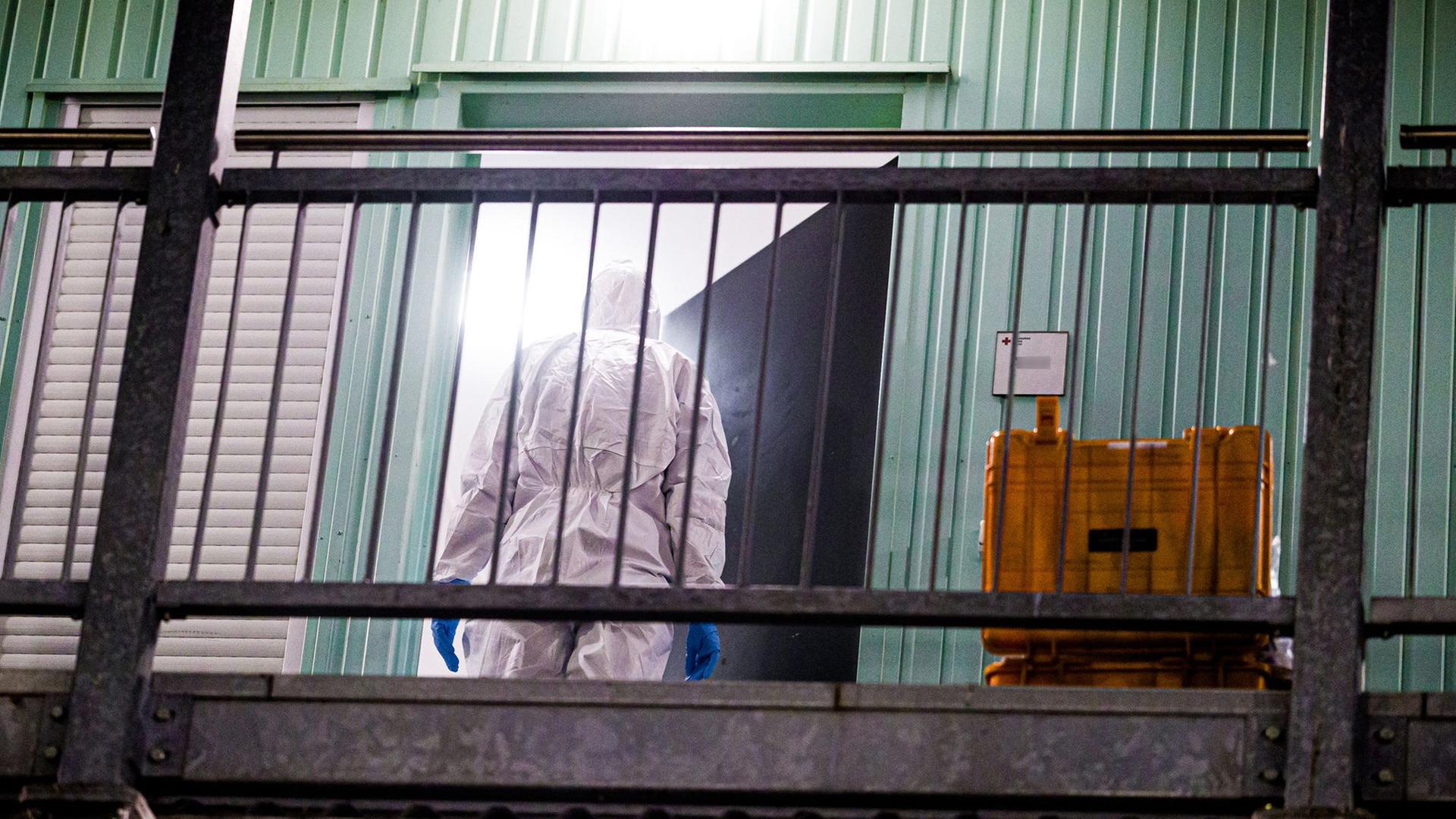 Eine Person im Schutzanzug steht in einer Tür einer Flüchtlingsunterkunft. | Moritz Frankenberg/dpa 