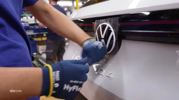 Ein VW-Logo wird an ein Auto angebracht.