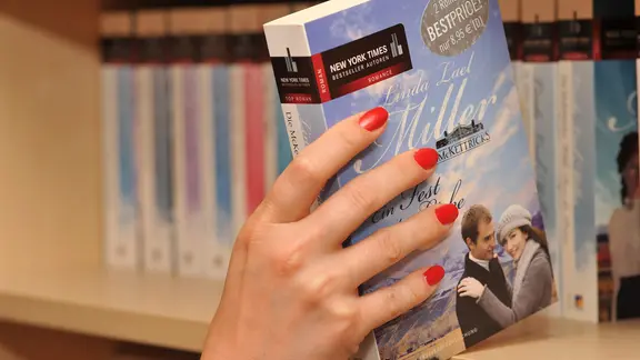 Eine Hand nimmt eine Buch aus dem Buchregal