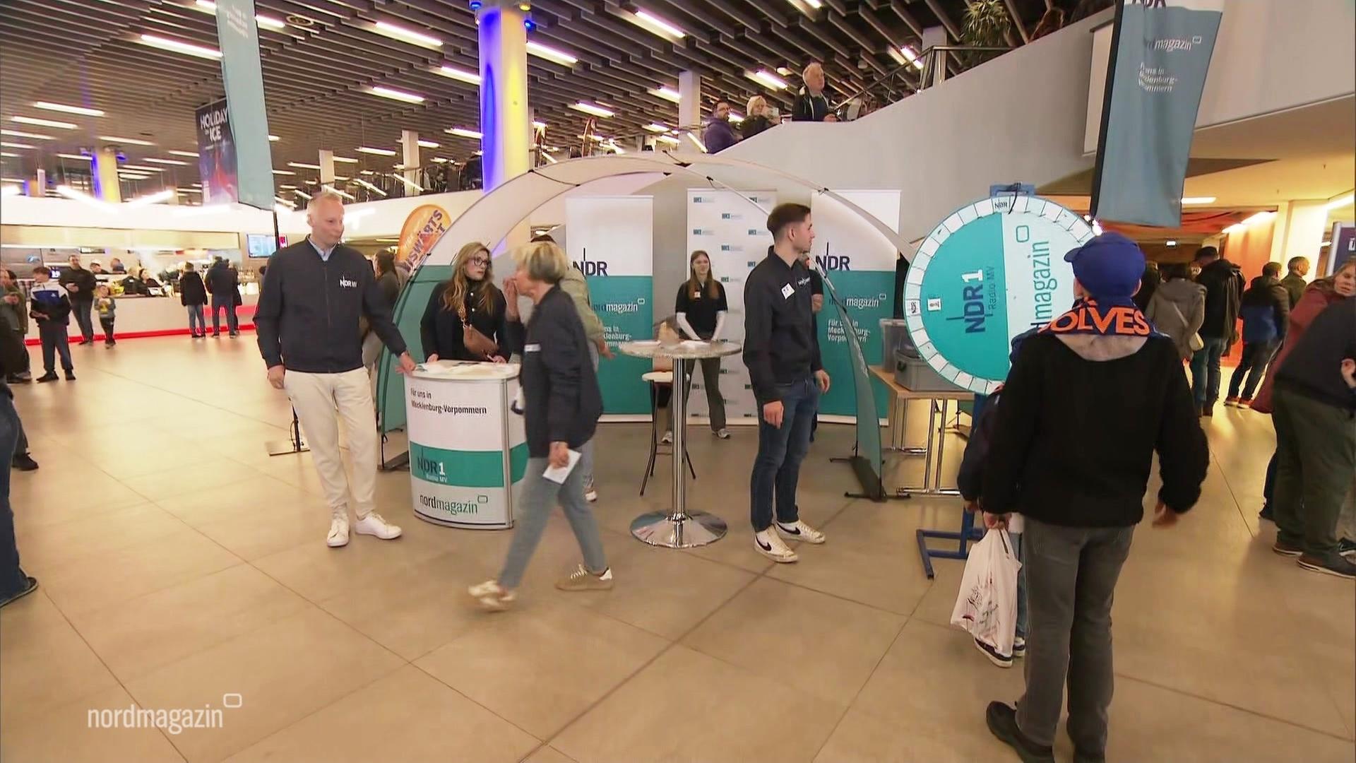 Ein Stand von NDR 1 MV mit Glücksrad in der Halle in Rostock. | Screenshot
