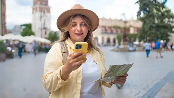 Eine Frau hält einen Stadtplan in der Hand und sieht auf ihr Smartphone.