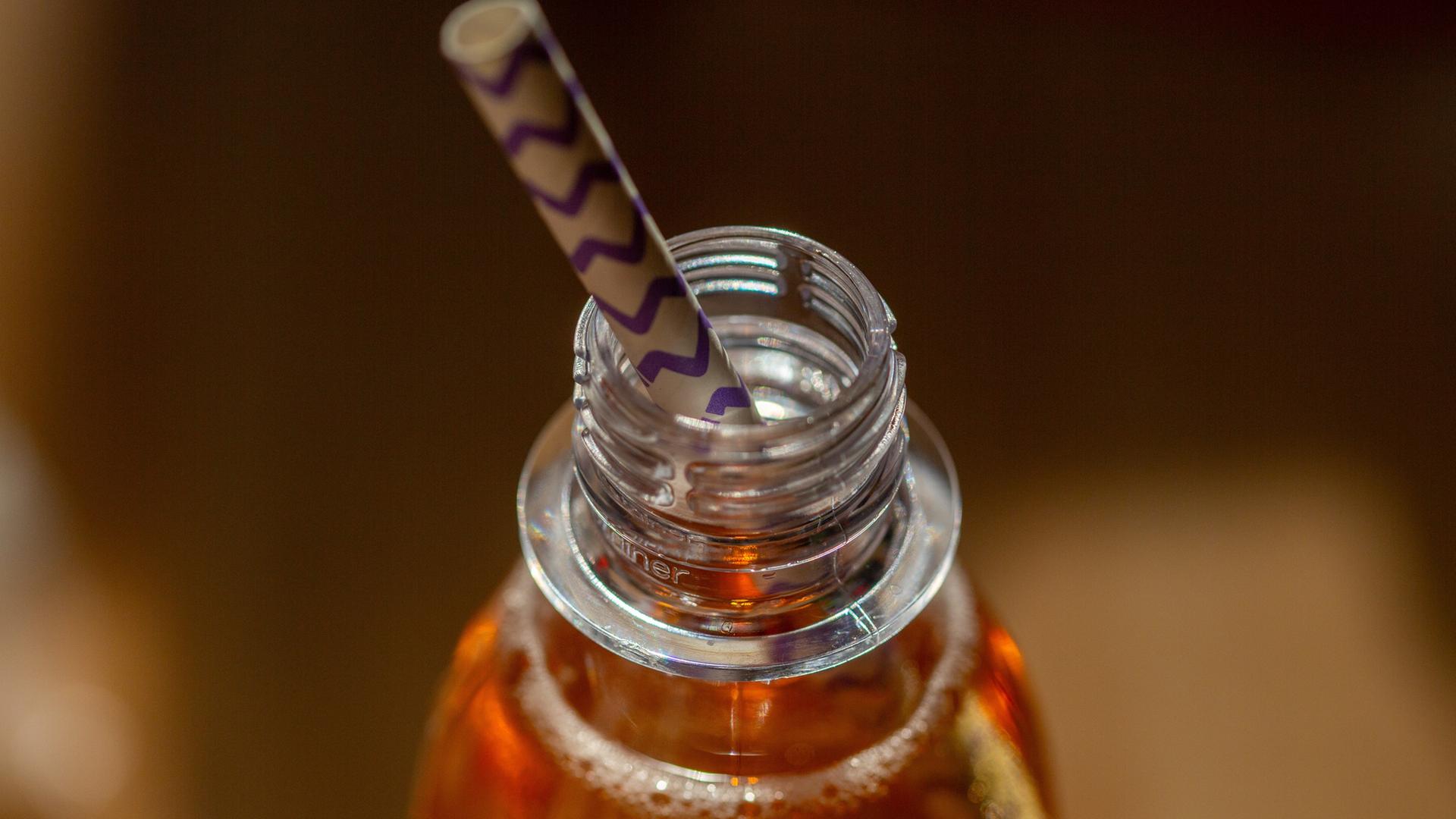 Eine geöffnete Flasche mit einem zuckerhaltigen Erfrischungsgetränk steht auf einem Tisch, in der Öffnung steckt ein Trinkhalm. | picture alliance / dpa, Fernando Gutierrez-Juarez