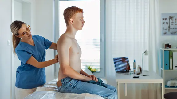 Eine Hautärztin schaut sich den Rücken eines Patienten an.