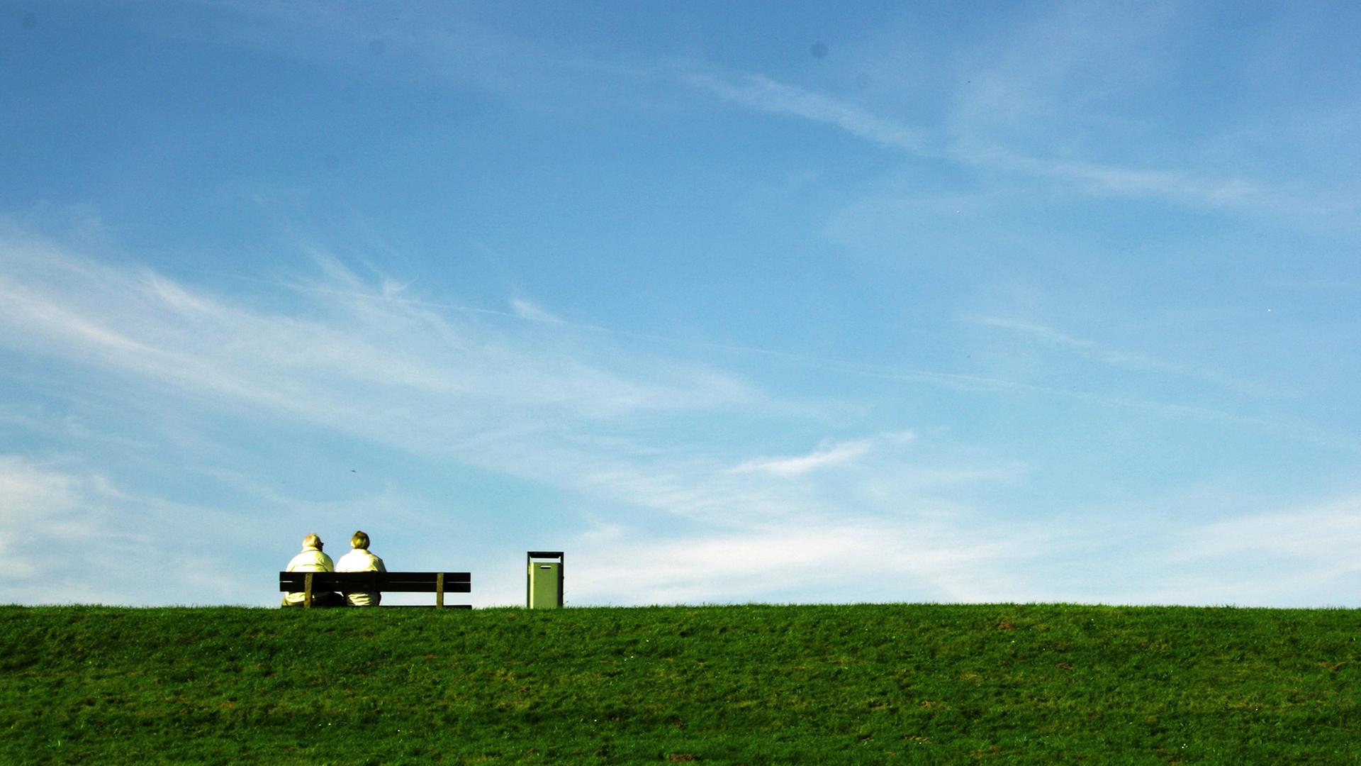 Zwei Männer sitzen auf einer Bank auf einem Deich. | photocase.de, micjan