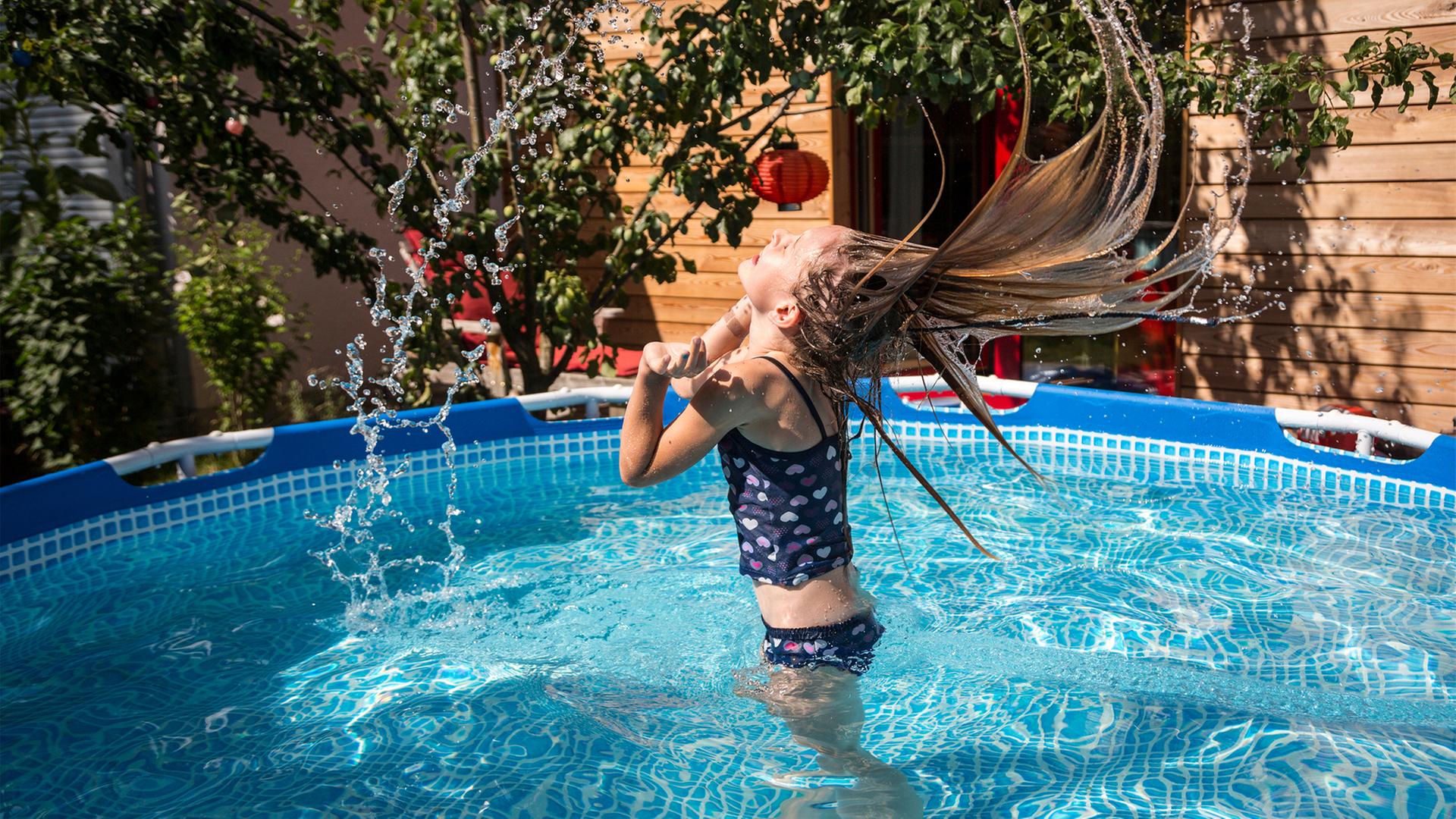 Ein Mädchen badet in einem Gartenpool, wirft ihren Kopf in den Nacken und schleudert Wasser aus ihren langen Haaren. | photocase.de, Westend61