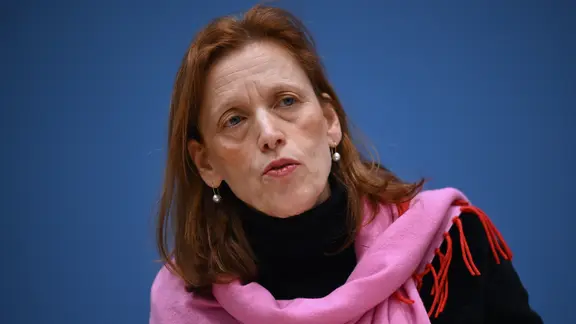 Eine Frau mit roten langen Haaren und rosafarbenem Schal schaut nach vorn.