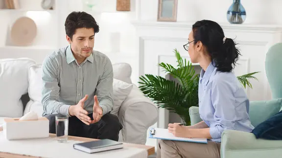 Ein Mann in einem Gespräch mit einer Psychotherapeutin in einem gemütlichen Raum.