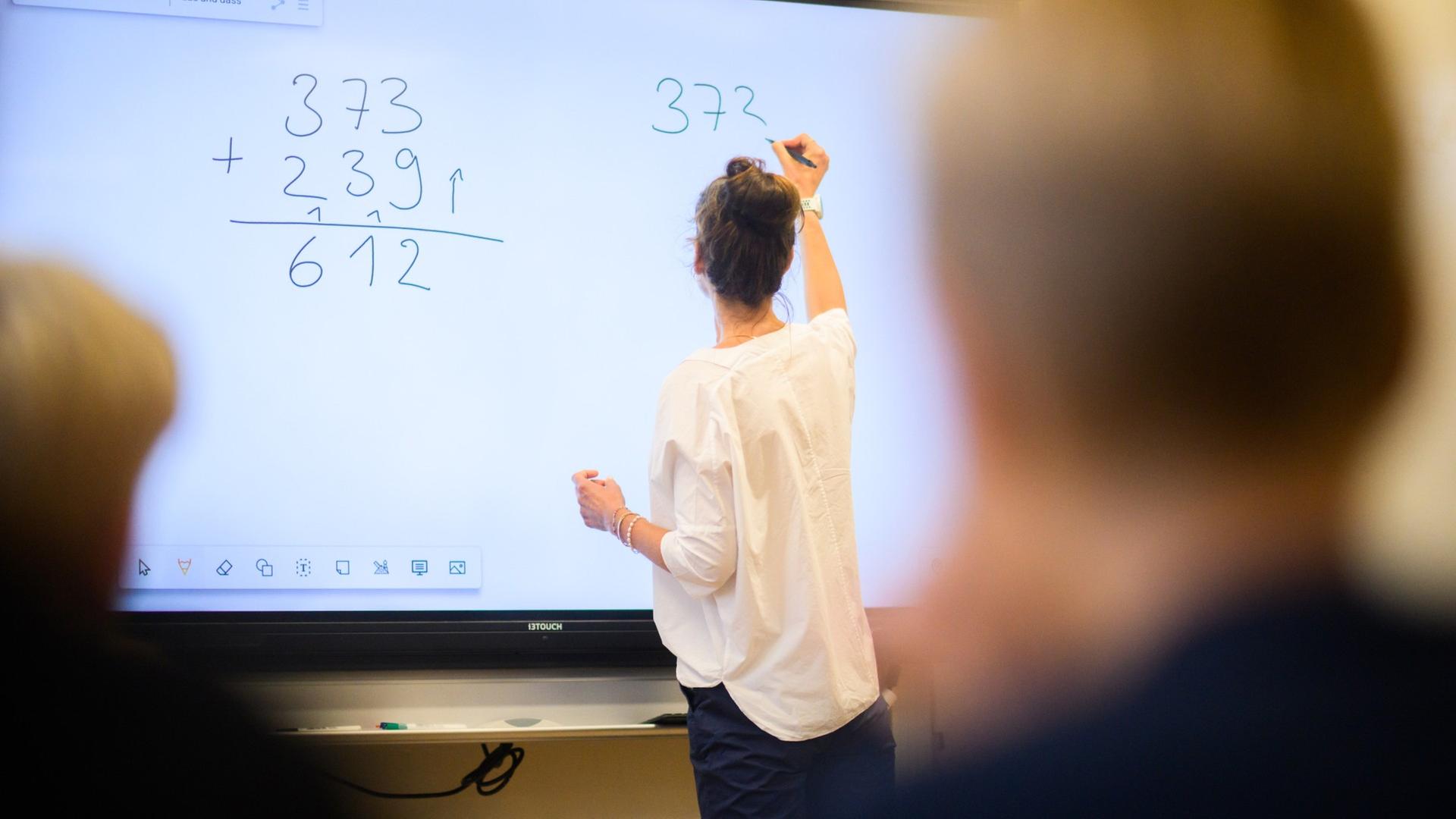Eine Lehrerin schreibt eine Mathematikaufgabe auf eine digitale Schultafel. | picture alliance/dpa/Julian Stratenschulte, Julian Stratenschulte