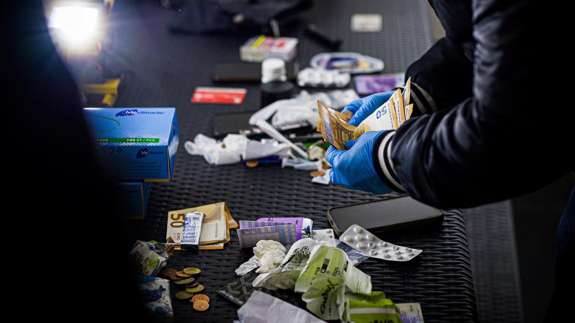 Ein Polizist zählt 50er-Geldscheine, auf einem Tisch liegen Utensilien aus Durchsuchungen. | picture alliance/dpa-Bildfunk, Moritz Frankenberger