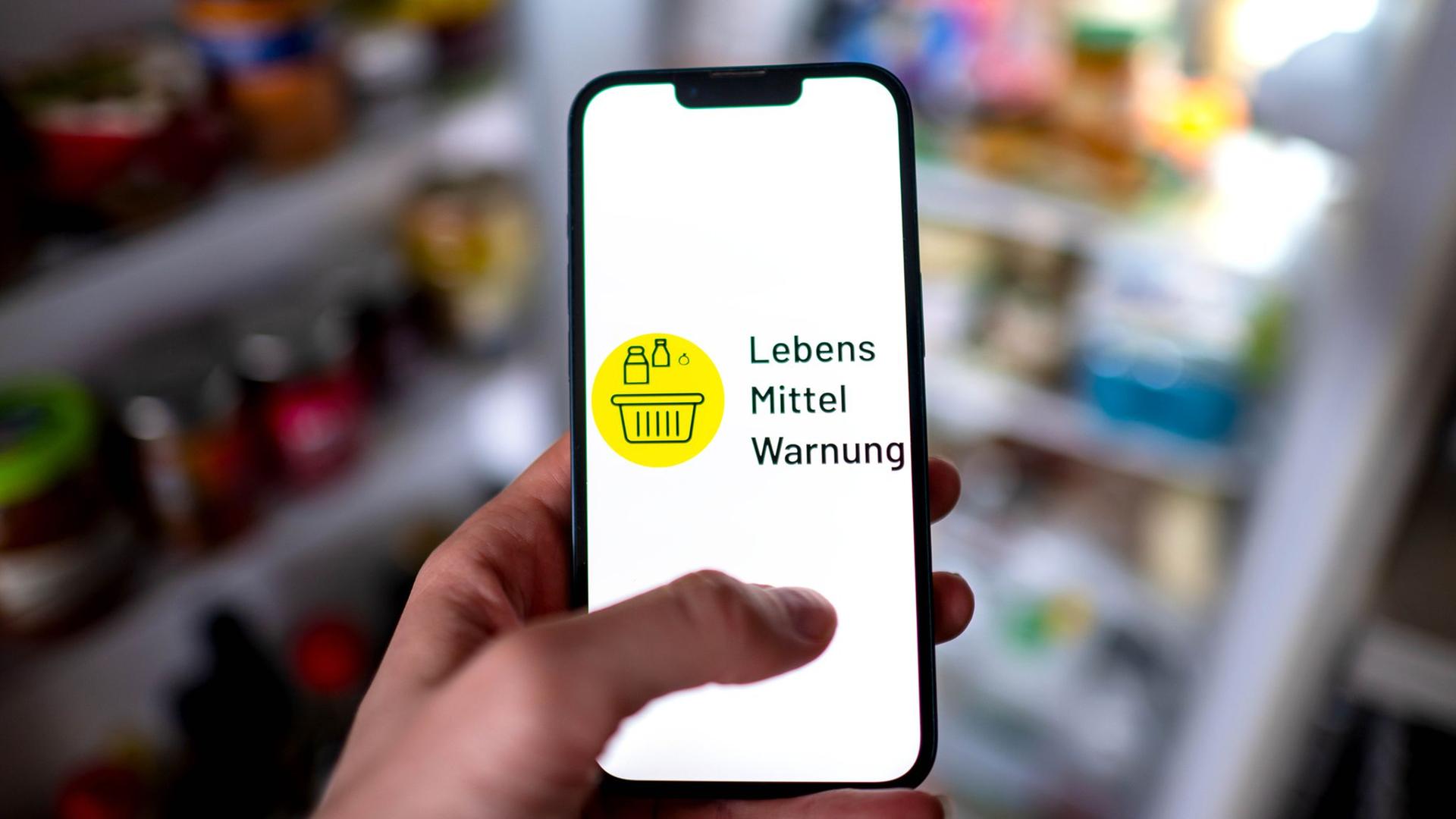 Die App Lebensmittelwarnung ist auf einem Smartphone vor einem Kühlschrank zu sehen. | dpa/Sina Schuldt