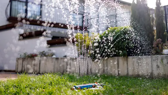 EIn Rasensprenger bewässert einen Garten.