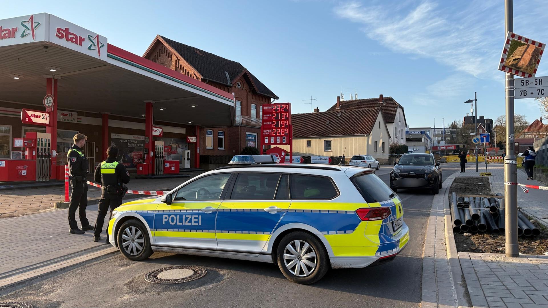 Ein Polizist und eine Polizisten stehen vor einer Absperrung, im Hintergrund sind eine Tankstelle und eine Wohnsiedlung zu sehen | NDR/Nord-West-Media TV & Nachrichten GmbH 