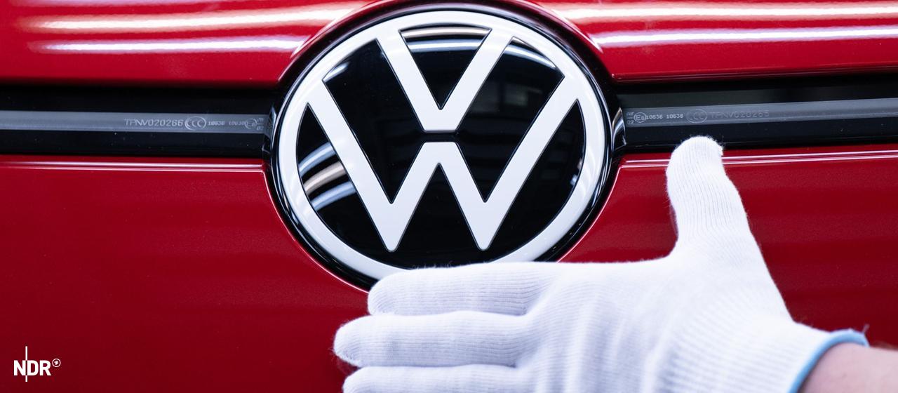 Eine Hand liegt unter dem VW-Logo auf einem Auto.